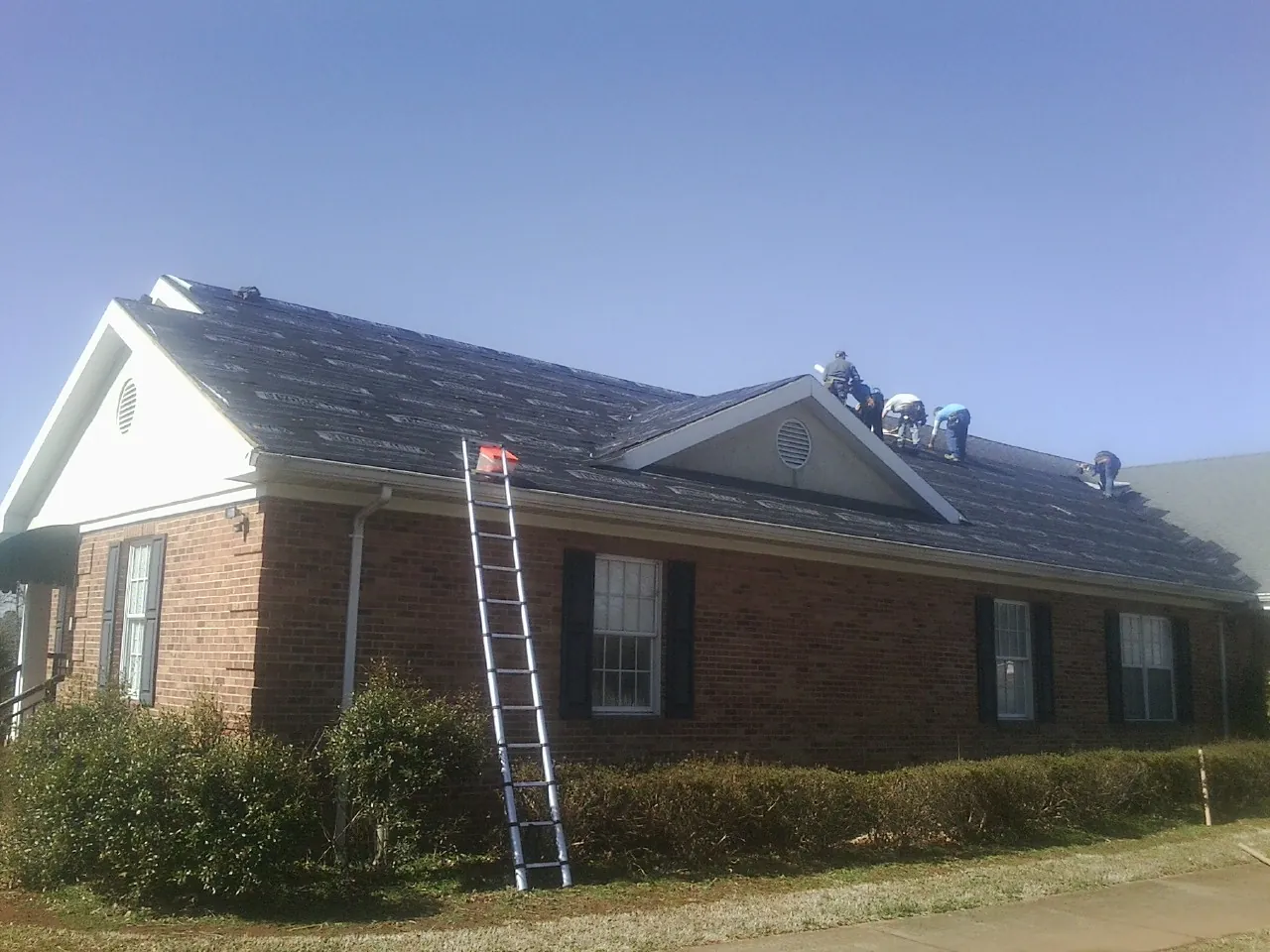 Crew tearing shingles off a brick ranch roof with a ladder set — Metal Roof Repair work by our crew in Festus