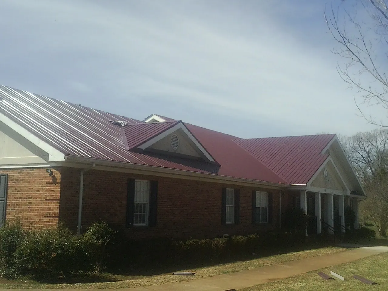 Red metal roof with gabled entries on a long brick building, from a Hail Damage Roof Repair job in Festus