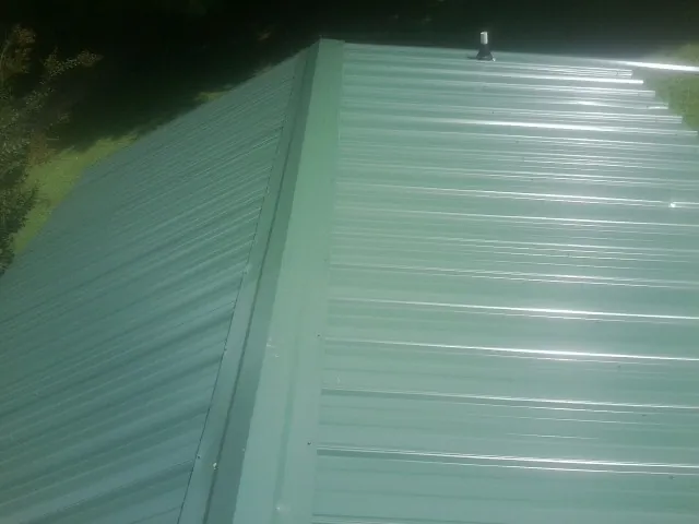 New green metal panels meeting at the ridge of a roof — Flat Roof Repair work by our crew in Festus